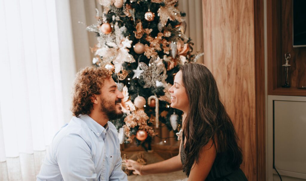 A man and a woman exchange Christmas gifts for him and her while sitting in front of a holiday tree in their house in Alameda, California. They are happy and facing each other.
