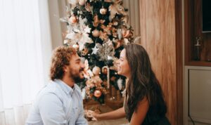 A man and a woman exchange Christmas gifts for him and her while sitting in front of a holiday tree in their house in Alameda, California. They are happy and facing each other.