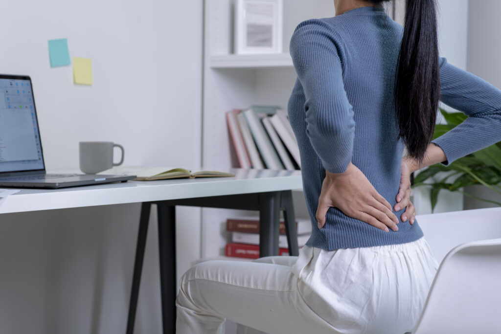 Woman massaging lower back experiencing sciatic pain after sitting at work desk.